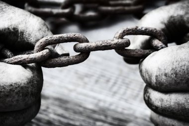 Eski paslı bir zinciri yırtmaya çalışan güçlü erkek elleri. Siyah beyaz fotoğraf.