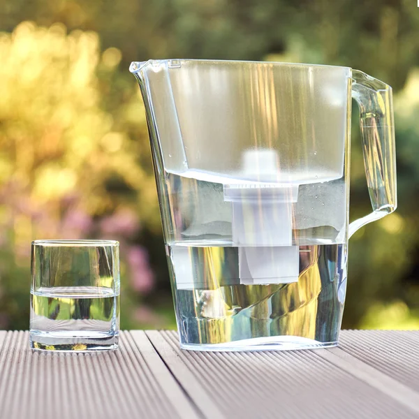 夏の庭の背景にクローズアップ水フィルターピッチャーと透明な水のきれいなガラス — ストック写真