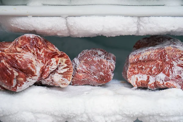 Large pieces of red meat in a freezer with a big quantity of frozen ice and snow