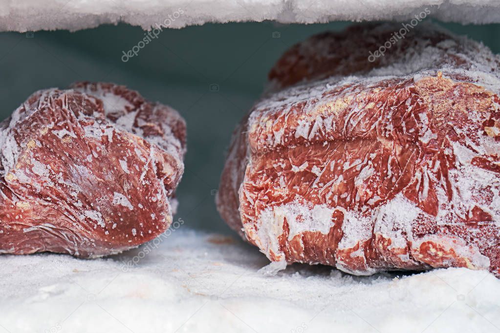 Large pieces of red meat in a freezer with a big quantity of frozen ice and snow