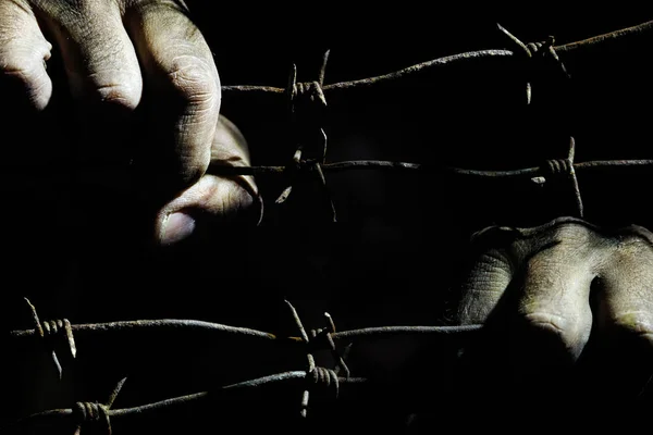 Sucias manos masculinas sostienen alambre de púas oxidado estirado en la oscuridad —  Fotos de Stock