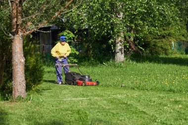 Yaşlı kadın kırsal bir elektrikli çim biçme makinesi ile çim çimlerini biçiyor