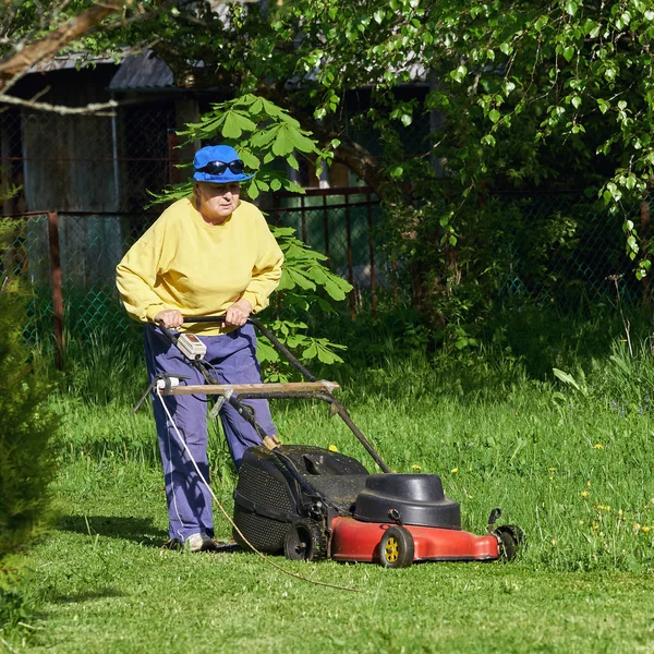 Mujer mayor corta el césped con una cortadora de césped eléctrica en el campo — Foto de Stock