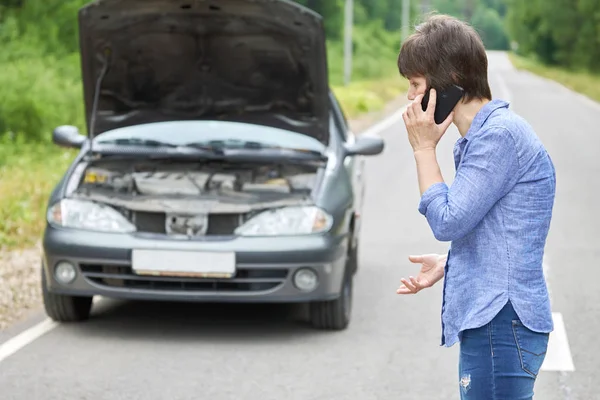 Worried woman talks on the phone near her old broken car on the road — Stock Photo, Image