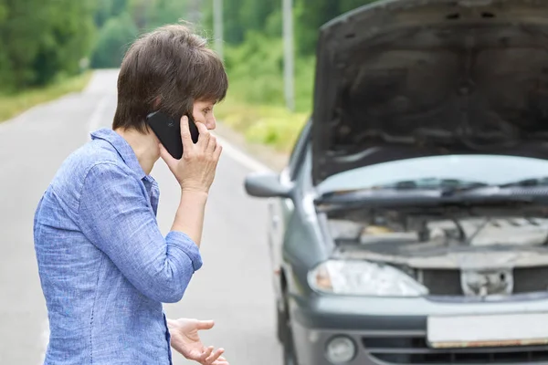 Worried woman talks on the phone near her old broken car on the road — Stock Photo, Image