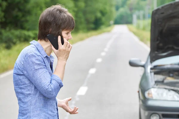 Mulher preocupada fala ao telefone perto de seu velho carro quebrado na estrada — Fotografia de Stock