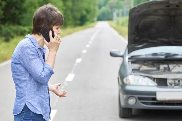Martwi kobieta rozmawia na telefon w pobliżu jej stary zepsuty samochód na drodze — Zdjęcie stockowe