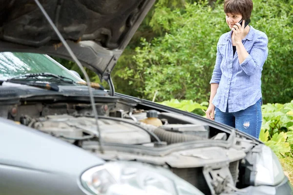 Mulher preocupada fala ao telefone perto de seu velho carro quebrado — Fotografia de Stock