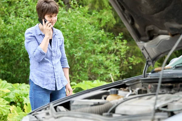 Mulher preocupada fala ao telefone perto de seu velho carro quebrado — Fotografia de Stock