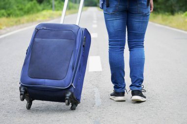 Kot pantolon ve spor ayakkabı lı kadın bacakları ve tekerlekli bir seyahat çantası yolda yürüyor