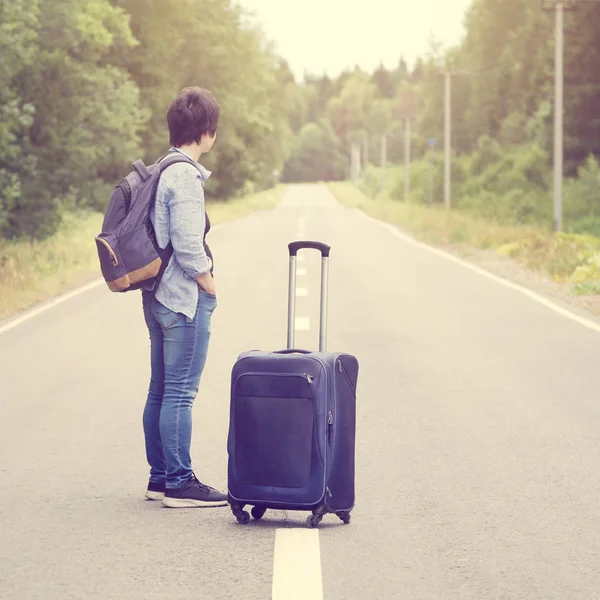 Frau mit Gepäck steht mitten auf einer asphaltierten Straße und wartet auf einen Transport — Stockfoto