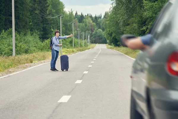 Middle-aged woman with a travel bag hitchhiking on the rural road in summer — Stock Photo, Image