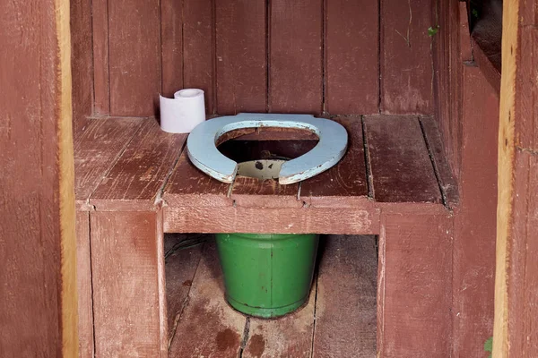 País banheiro de madeira com um balde de metal e um rolo de papel — Fotografia de Stock