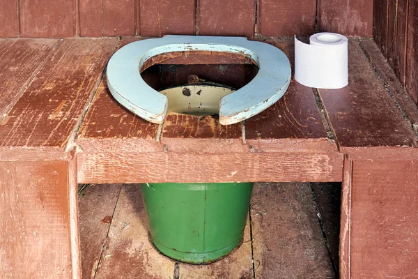 Assento sanitário de um banheiro de madeira de país com um balde metálico e um rolo de um papel — Fotografia de Stock
