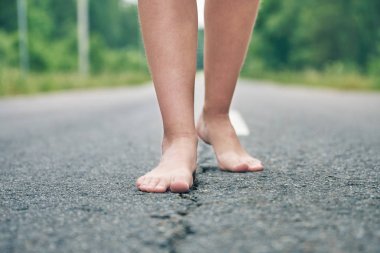 Asfalt yol boyunca yürüyen bir genç kızın çıplak ayaklar