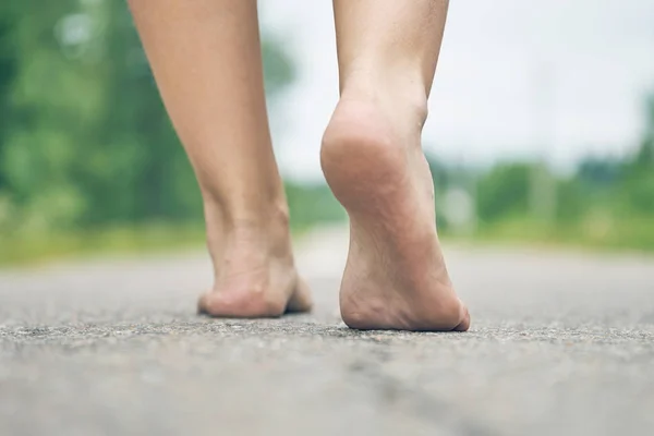 Les pieds nus de la jeune fille marchant le long de la route asphaltée se rapprochent. Vue arrière — Photo