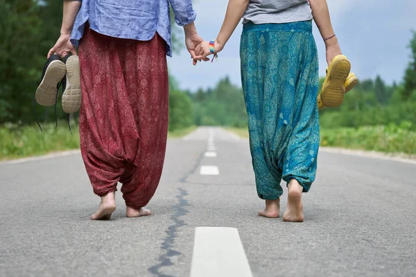 Barfuß gehen eine erwachsene Frau und ein junges Mädchen Hand in Hand die asphaltierte Straße entlang — Stockfoto
