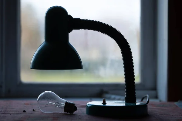 Old electric lamp with burned-out light bulb lying on the table in front of a window. Concept of an electric network crash. Depression, sadness,poverty,end.