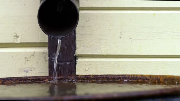 Voda tekoucí z plastového odtokového potrubí do kovového sudu po dešti. — Stock video