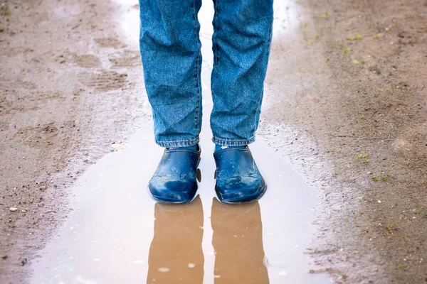 一个穿着橡胶靴的女人站在乡村路上脏兮兮的水坑里的腿 — 图库照片