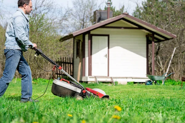 中年男人春天用电动割草机割草在他乡下房子的后院 — 图库照片