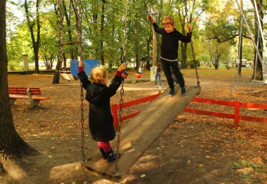 Çocuklar parkta büyük bir ağaçta salıncakta sallanıyor.
