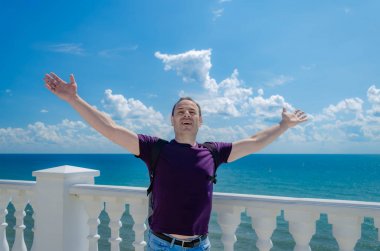 Gülümseyen yaşlı adam elleriyle denize karşı duruyor.