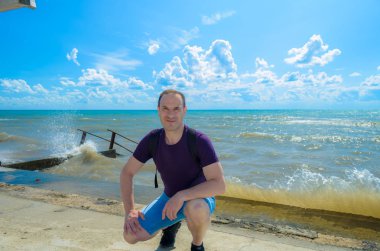 50 yaşındaki adam arka planda deniz ile, sahilde güzel bir gün, bir kıyıda oturan.