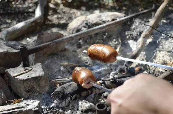 Saucisses rôties sur un bâton au-dessus du feu de camp ouvert. Préparation des aliments en extérieur . — Photo