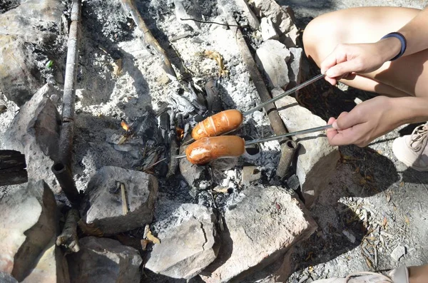 Salsichas assadas num pau sobre a fogueira. Preparação alimentar ao ar livre . Fotos De Bancos De Imagens