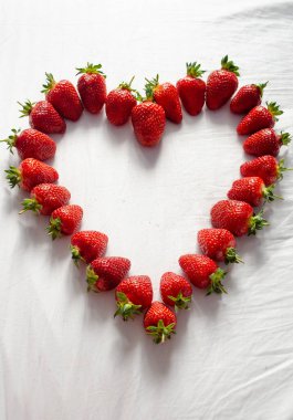 Olgun çilekler kalp şeklinde beyaz bir arka planda serilmiştir.