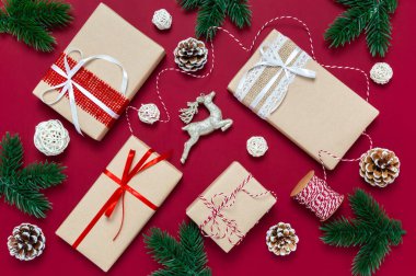 Noel hediyesi kutuları, çam kozalakları, ağaç dalları ve arka planda kırmızı arka plan manzaralı ren geyikleri. Noel hediyelerini paketliyorum. Kış tatili teması. Mutlu Noeller ve mutlu yıllar.