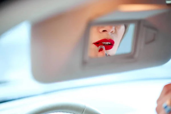 Hermosa chica conduciendo un coche pinta los labios con lápiz labial rojo Imagen De Stock