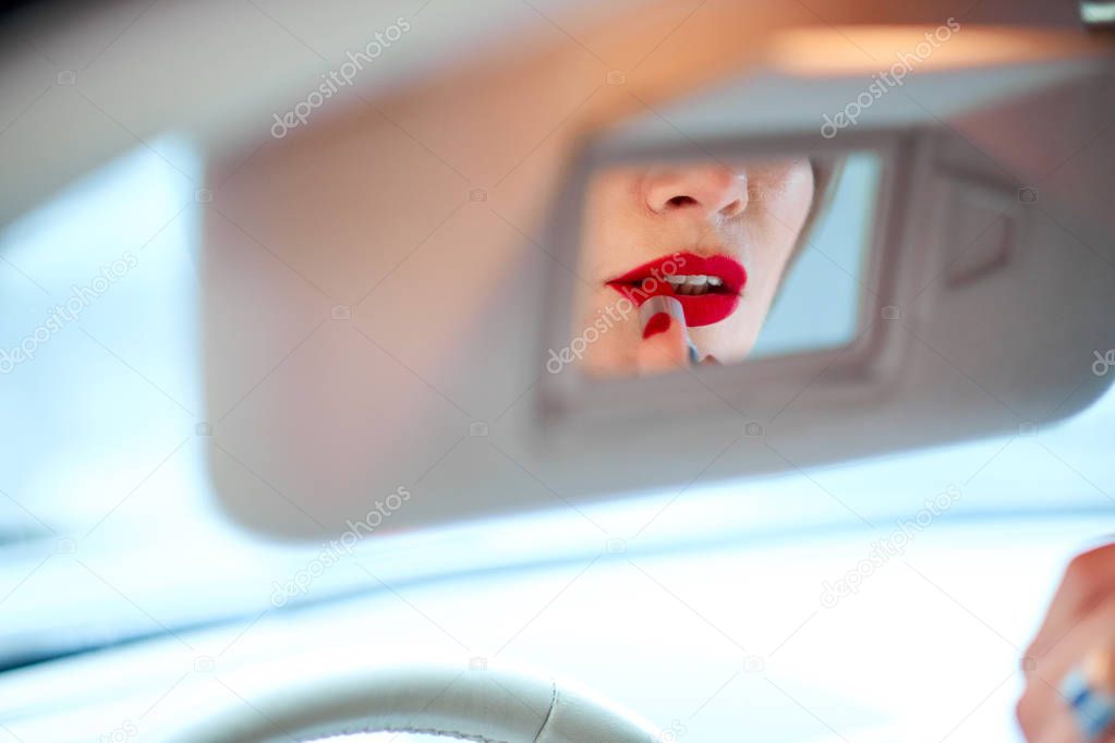 Beautiful girl driving a car paints lips with red lipstick