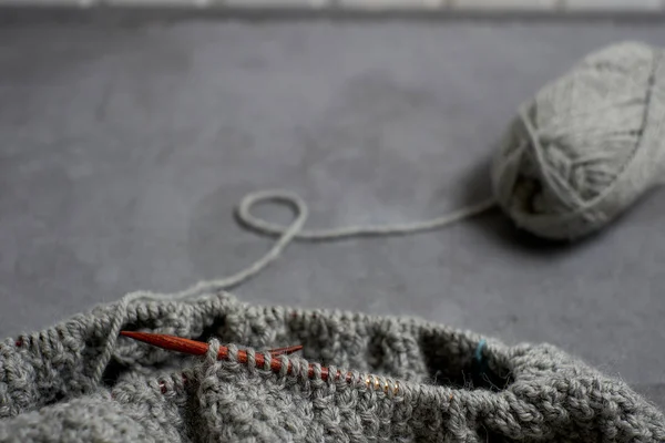 Серый незавершенный свитер с клубком нитей на сером фоне — стоковое фото