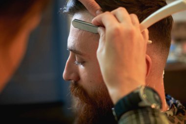 Bir hairdresses çalışması için çekici bir genç sarışın erkek kuaför dükkanında kapatın. Ustura ile tıraş sakalını, stil yapıyor