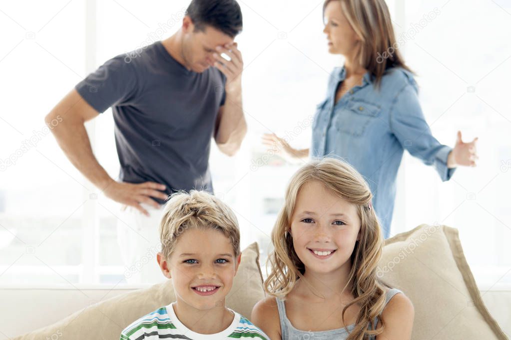 portrait of happy children sitting on sofa in foreground - parents arguing in background - family relationships concept