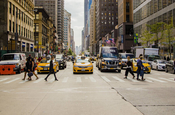 New York, USA- September 2017 Manhattan street with yellow taxi crossing the road and people