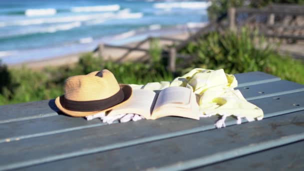 Libro, chal y un sombrero en la mesa con olas azules en el fondo . — Vídeo de stock