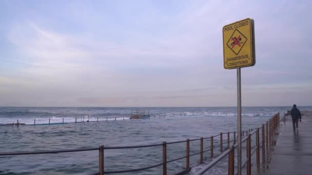Una señal de advertencia a lo largo de una piscina de roca del océano desierta informa que la piscina está cerrada. — Vídeo de stock