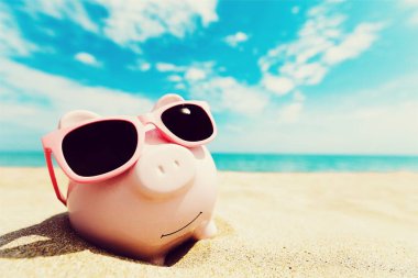 Kumlu plajda güneş gözlüğü ile Piggy banka 