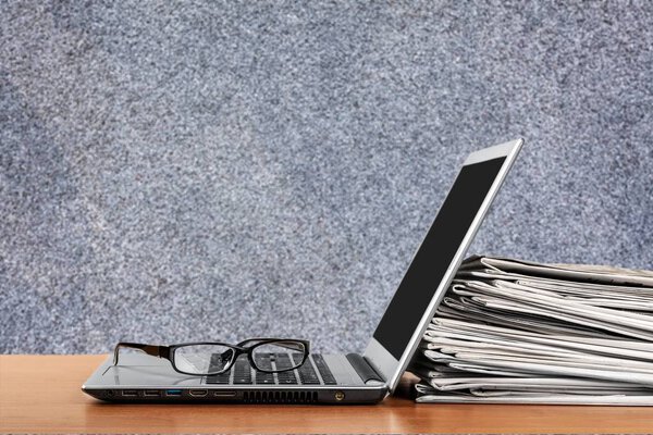 Laptop and black glasses ans stack of newspapers 