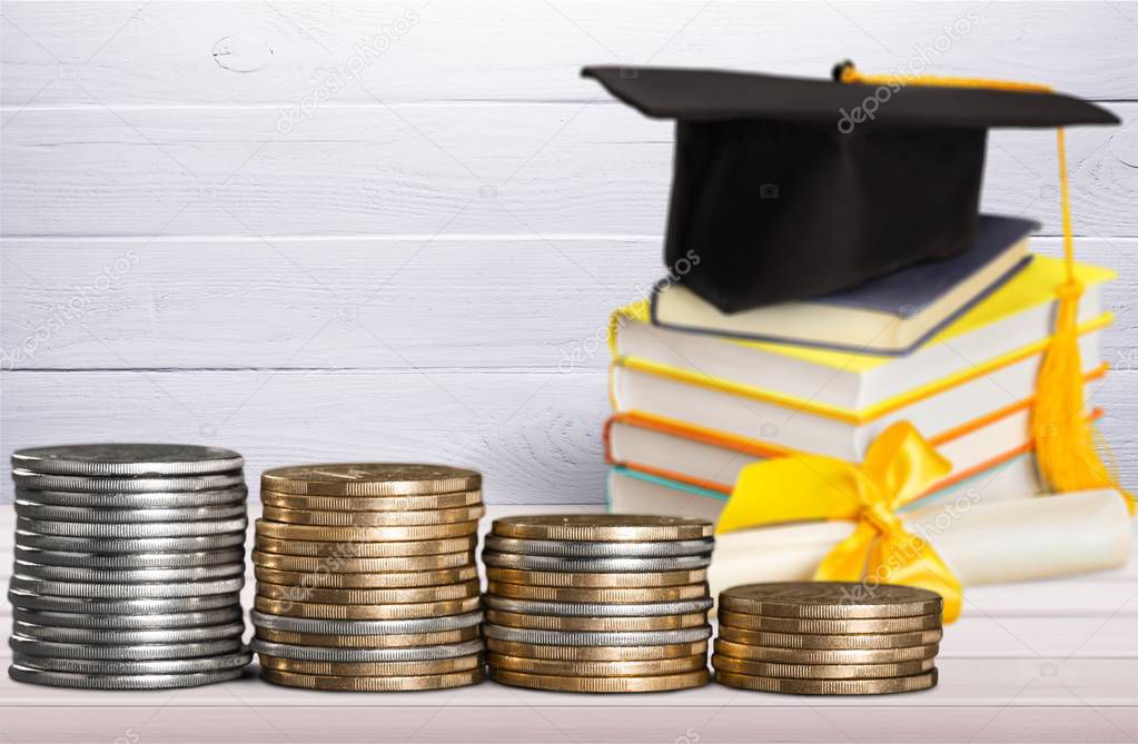 Graduation hat and stacked coins on wooden table 