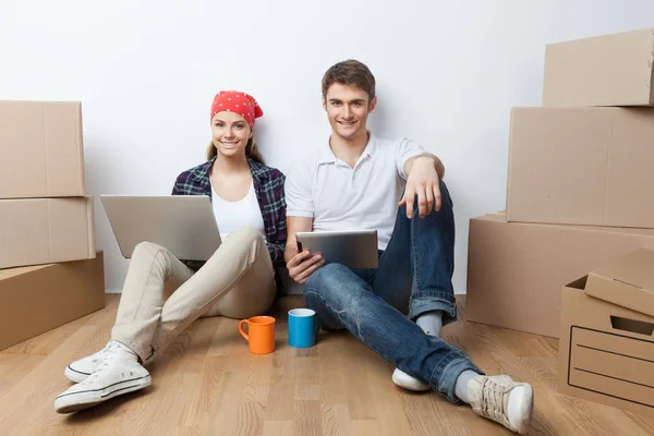 Junges Paar sitzt mit Kisten auf dem Boden und benutzt Laptop und Tablet — Stockfoto