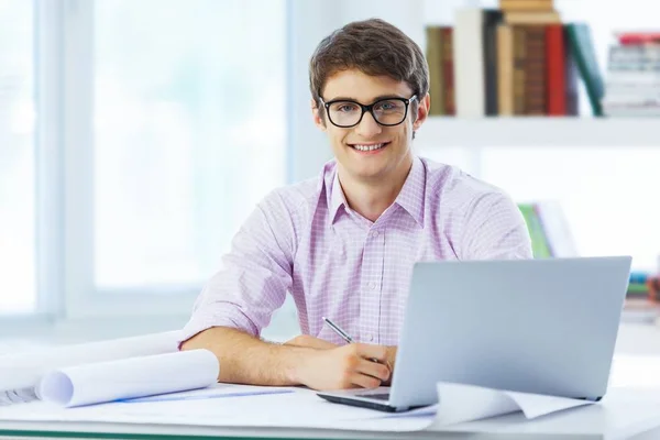 Retrato de un joven empresario sonriente trabajando en planos en la oficina —  Fotos de Stock