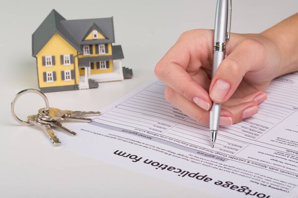 Кредитный договор на недвижимость, женский документ для подписания, ключи от дома на столе
