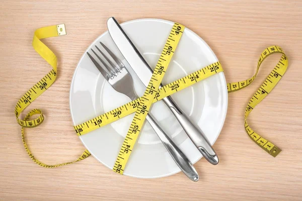Zdrowe jedzenie lub diety koncepcji. pusty płyta, widelec i nóż owinięte w taśma miernicza — Zdjęcie stockowe