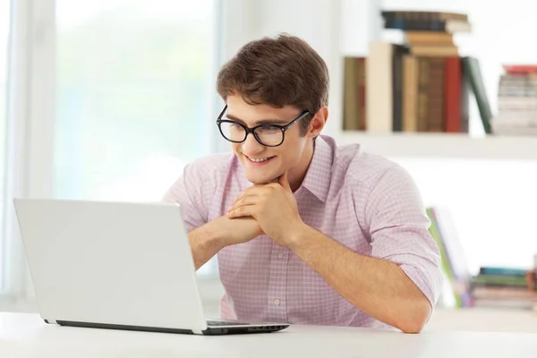 Estudante sorrindo trabalhando no laptop com estantes em segundo plano — Fotografia de Stock