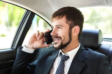 Zarif işadamı lüks arabaya seyahat cep telefonda konuşurken gülümseyen
