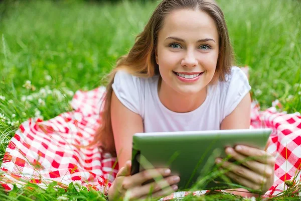 Glückliche junge Frau mit digitalem Tablet auf Gras liegend — Stockfoto